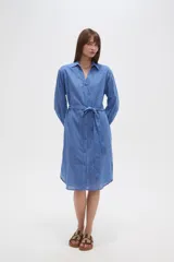 Vestido camisero de algodón color azul, de corte ancho y manga larga, con cuello camisero y lazo ajustable a la cintura.