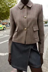 Blazer corto de corte estructurado con cuello solapa, manga larga y hombreras. Presenta cierre frontal con botones metálicos y dos bolsillos delanteros de plastrón con solapa. Diseño con estampado de cuadros tipo príncipe de gales.