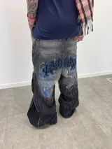 Jean de corte amplio en color negro con efecto acid wash. Presenta cierres laterales metálicos que permiten ajustar la silueta entre corte recto, oxford o baggy. Incluye una estampa gráfica de gran tamaño en la parte trasera con detalles bordados, bolsillos amplios y una etiqueta de cuero legítimo en la cintura.