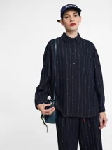 Camisa azul marino con botones en la parte delantera y bolsillo en el pecho. Diseño de rayas verticales bordadas con hilo metálico.