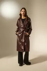 Trinchera de eco-cuero en color bordó, con diseño de doble botonadura, solapas amplias y cinturón ajustable en la cintura. Presenta mangas largas con detalles en los puños y bolsillos laterales.