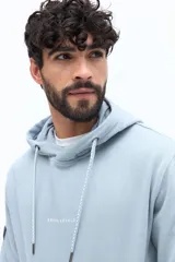 Canguro de algodón color celeste claro, con capucha ajustable mediante cordones trenzados blancos y bolsillo canguro frontal. Presenta un pequeño texto estampado en el pecho.