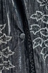 Kimono de terciopelo gris con acabado texturizado, cuello redondo y manga larga. Presenta bordados florales en hilo negro y metalizado, bolsillos delanteros y cierre frontal.