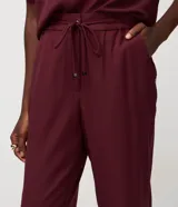 Pantalón de crepé rojo, modelo estilo pijama, de corte fluido, con cintura elástica y lazo de ajuste con terminales metálicas. Cuenta con bolsillos laterales y cierre frontal con cremallera y botón.