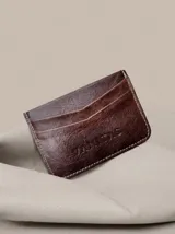 Tarjetero compacto de cuero marrón con ranuras para tarjetas en ambos lados y costuras visibles en los bordes.