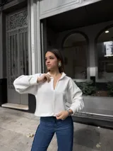 Buzo blanco de corte holgado con cuello polo y cierre frontal parcial. Presenta mangas largas amplias y un diseño de silueta relajada, confeccionado en tejido suave.