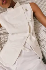 Top de denim blanco sin mangas, con cuello mao y cierre frontal cruzado con trabillas y botones metálicos.