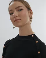 Polera gris de tejido de punto con cuello redondo y mangas largas. Presenta detalle de botones metálicos en los hombros y puños.