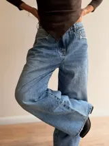 Pantalón de jean estilo palazzo en tono celeste medio, con corte amplio y recto. Presenta detalles de roturas sutiles en los bolsillos y ruedo, con cierre frontal y bolsillos laterales.