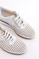 Zapatillas acordonadas color dorado con capellada de cuero calado, base blanca y detalles en cuero blanco en el talón.
