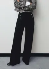 Pantalon de vestir negro de corte wide leg y tiro medio. Presenta un diseño largo con detalle de botones metálicos plateados en la parte frontal y cierre de cremallera lateral.