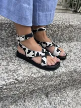 Sandalia de cuero color plateado con plataforma. Presenta tiras cruzadas en la parte delantera, una tira con agarre para el dedo gordo y una pulsera ajustable con hebilla en el tobillo.