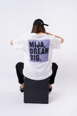 Remera negra de corte oversize con estampado frontal que dice "MIJA DREAM BIG" en tipografía blanca y rosa.