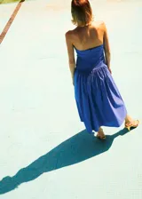 Vestido midi azul sin tirantes, con escote palabra de honor fruncido en el pecho, corte ajustado en el torso y falda amplia de corte evasé.