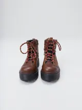 Bota de estilo trekking con diseño multicolor en tonos marrón, azul y detalles en rojo. Presenta plataforma de goma dentada, cordones tipo cuerda de escalada y cuello acolchado.