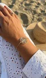 Pulsera dorada ajustable con medalla de San Benito redonda, calada y decorada con circonias brillantes.