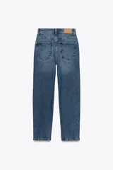 Jeans de mujer, tiro alto, corte Mom Fit con pierna slim y largo tobillero. Denim azul medio con efecto desgastado y lavado. Presenta cinco bolsillos y cierre frontal con cremallera y botón.