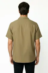 Camisa de manga corta color verde militar, con cuello camisero y cierre frontal de botones.