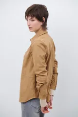 Camisa de estilo casual confeccionada en material tipo gamuza color marrón, con cuello clásico, cierre frontal con botones y costuras a la vista en tono contrastante.