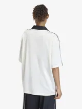 Camiseta de fútbol de corte oversize, color blanco con detalles en negro. Presenta cuello tipo polo con escote en V, mangas cortas con las icónicas tres tiras de Adidas en los hombros y estampado gráfico frontal inspirado en la estética deportiva de los años 90.