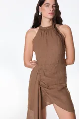 Vestido corto de lino celeste, con escote halter, falda drapeada asimétrica y cierre invisible en el lateral.