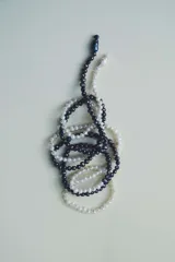 Collar compuesto por múltiples hilos de cuentas de vidrio que imitan perlas en tonos blanco y negro, entrelazados en un diseño dinámico.