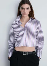 Camisa crop de mangas largas con puños abotonados, cuello camisero y cierre frontal con botones. Diseño a rayas verticales blancas y azul marino.