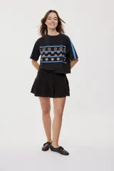 Remera blanca de manga corta, con cuello redondo, calce relajado y estampado frontal con motivos gráficos de soles y símbolos marinos en tonos rosados y bordo, además de líneas horizontales.