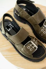 Sandalias negras de cuero con diseño de plataforma dentada, tiras ajustables con hebillas metálicas y detalle de tachas plateadas en el lateral de la suela.