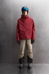 Cazadora deportiva de esquí con diseño bicolor en tonos negro y verde oliva. Presenta capucha amplia con visera, cierre frontal con cremallera termosellada, bolsillos frontales y en manga con cierres impermeables, y aberturas de ventilación en las axilas. Incluye faldón interior antinieve, puños ajustables y tecnología de rescate RECCO.
