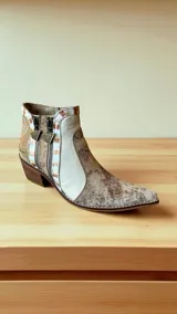 Bota corta de cuero con diseño jaspeado en tonos cobre y natural, con detalles pintados a mano. Cuenta con punta fina, taco cuadrado, doble cierre lateral con tiradores metálicos decorativos y costuras visibles en el borde de la suela.
