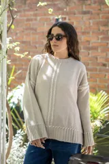 Sweater oversize de tejido de punto color beige, con cuello a la base y mangas largas acampanadas. Presenta detalles bordados a mano en color blanco en el frente, hombros y ruedo.