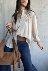Camisa de color beige, con mangas largas y detalles bordados en el pecho y los hombros. Presenta cierre frontal con botones y cuello camisero.
