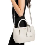 Bolso de mano tipo satchel color beige claro, con textura de cuero granulado y herrajes dorados. Presenta asas superiores rígidas y una correa cruzada ajustable y removible. Incluye un charm colgante decorativo con el logo de la marca.