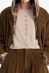 Blazer de pana marrón con solapas clásicas y botones oscuros. El forro de las mangas y la capucha superpuesta son de tela a cuadros en tonos marrones y beige.