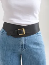 Cinturón tipo faja ancho de color negro, confeccionado en cuero sintético, con hebilla metálica rectangular en tono dorado antiguo.