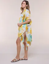 Kimono de gasa ligera con estampado floral en tonos amarillos, celestes, blancos y marrones, de manga corta amplia y diseño abierto con detalle de borlas en el ruedo asimétrico.