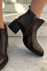 Bota corta de cuero color bordó, con taco cuadrado negro y suela de plataforma. Presenta detalles de tachas metálicas plateadas a lo largo de la costura frontal y lateral, con cierre interno.