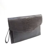 Sobre tipo carta de cuero color marrón oscuro con textura croco. Tiene un bolsillo interior y una correa de muñeca.