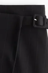 Short pollera negro de tiro alto con diseño cruzado tipo pareo y cinturón fijo con hebilla revestida. Presenta cierre oculto y cierre de corchete en un lateral.