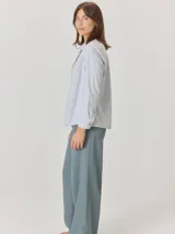 Camisa de algodón color gris claro, con cuello clásico y detalle de volados en la cartera frontal. Presenta mangas largas con puños abotonados y un corte recto.