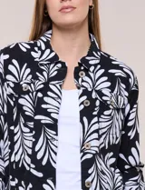Camperita de lino liviana, marca Dash, con estampado botánico de hojas en tonos azules, verdes y tostados sobre base blanca. Presenta cierre frontal con botones, cuello clásico y bolsillos aplicados en el pecho.