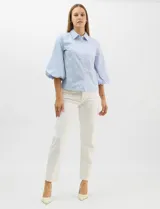 Camisa de algodón con patrón de rayas verticales, cuello camisero clásico y cierre frontal con botones. Presenta detalles metálicos aplicados en el frente y mangas, con mangas 3/4 abullonadas y ruedo recto.