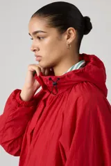 Campera parka roja estilo blouson con capucha ajustable, cierre frontal de botones a presión, bolsillos frontales con solapa y diseño holgado.