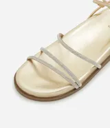Sandalia plana color dorado con acabado metalizado, diseño de tiras finas, algunas de ellas con incrustaciones de brillo, y cierre ajustable con hebilla al tobillo.