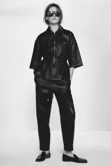 Chaqueta efecto piel color marrón, con cuello solapa, mangas por debajo del codo, cintura elástica, falsos bolsillos delanteros y cierre frontal con cremallera.