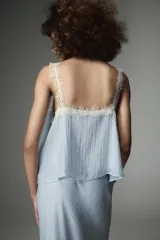 Top de estilo lencero color celeste, con escote recto y tirantes finos decorados con puntilla de encaje blanco. Presenta un detalle de encaje floral en el pecho.