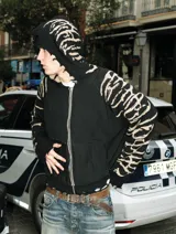 Hoodie con cierre frontal, confeccionado en tejido de punto 100% algodón. Es una prenda reversible con diseño de estampado gráfico en mangas y capucha, y presenta detalles de roturas intencionales en puños, ruedo y bolsillos.
