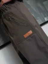Pantalón de neopreno impermeable forrado de polar, de corte holgado, color verde militar con paneles laterales en azul marino, bolsillos con cierre y parche de cuero sintético con logo.