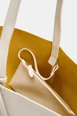 Bolso de hombro de piel en color blanco, con diseño tipo bucket, asa fija y detalle de tira colgante con nudo en el lateral.